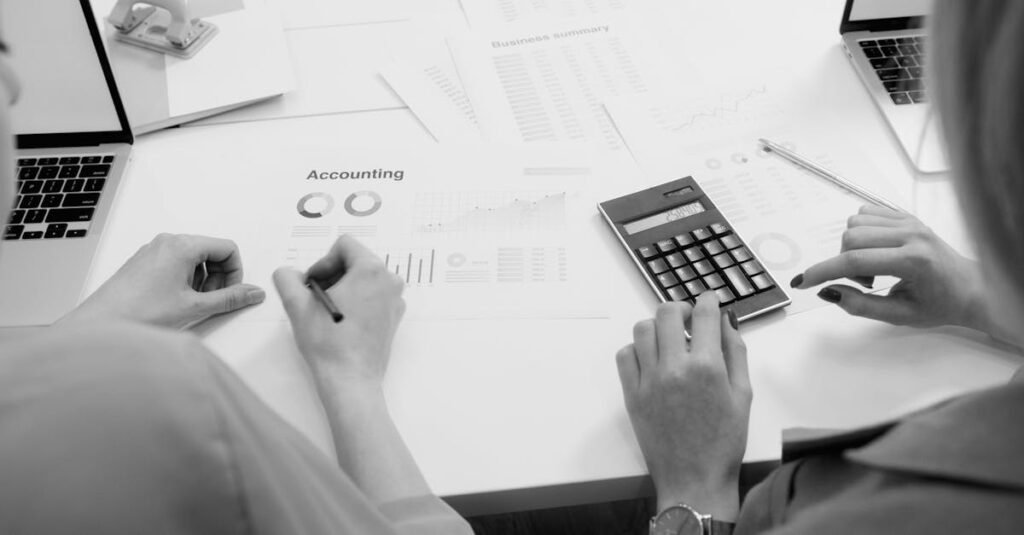 Black and white office scene featuring accounting documents, calculator, and laptops.